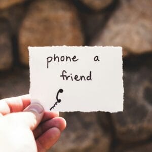 person holding piece of paper with phone a friend written text